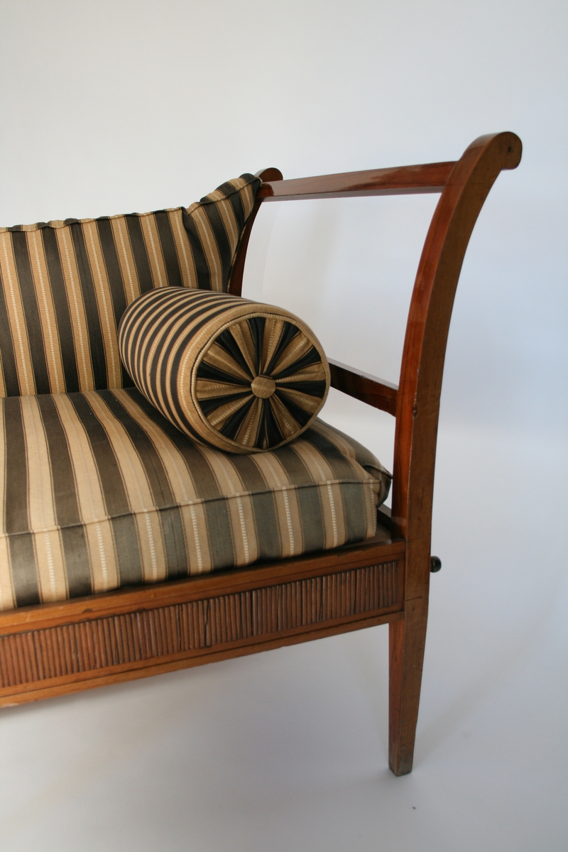 Empiresofa i mahogni. Rette spinkle bein, lett utsvingte vanger. Løs ryggpute og to løse pøller.