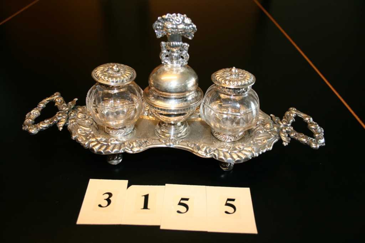 Avlangt sølvbrett, på fire føtter. To håndtak, innsvinget på midten, ornametikk med blomster og rocailler. Skål med bjelle festet midt på brettet, på hver side er det holdere til blekkhus og sandhus. Disse er av glass med kant og lokk av sølv.