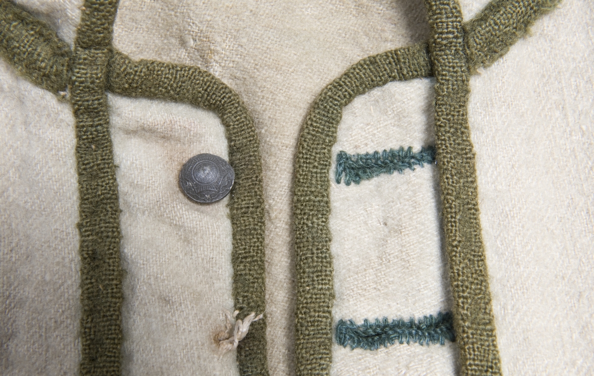 Hvit kjole av ull med grøn dekor av ull.
Midjen bak er markert med to garn dusker.