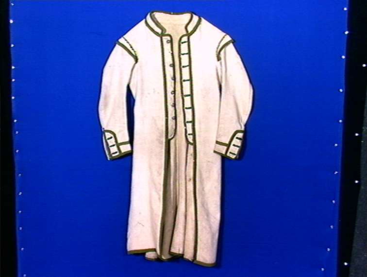 Hvit kjole av ull med grøn dekor av ull.
Midjen bak er markert med to garn dusker.