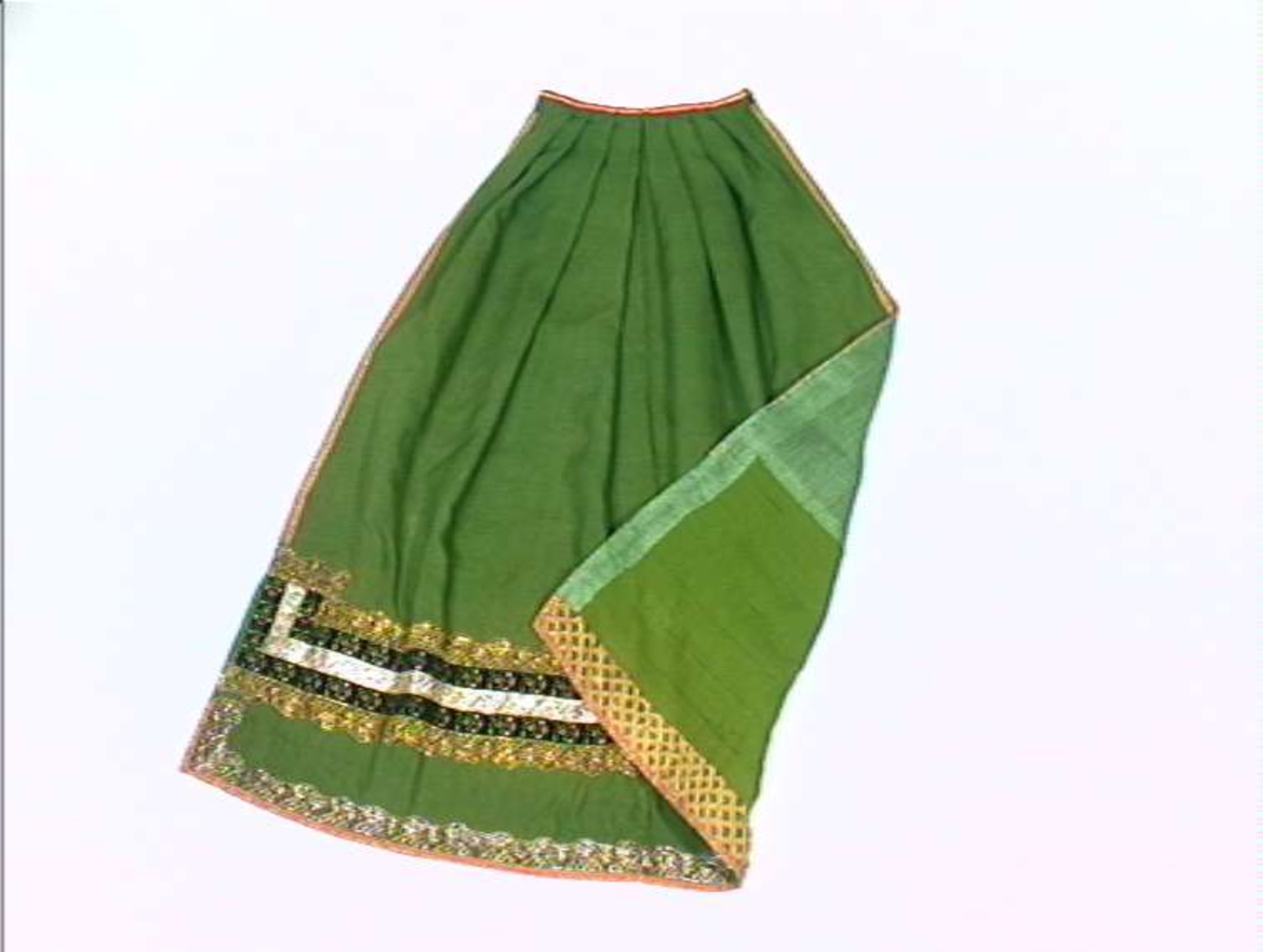 Grønt forkle av ull med dekor av metallblonder og bånd.