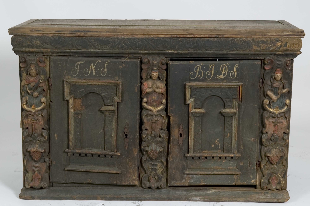 Skap med to dører. Skåret dekor, tre firgurer, en med slange i hendene, en med hendene i bedeposisjon, en med anker – representerer trolig hhv. visdom, tro og håp og visdom (tre av de syv dyder).