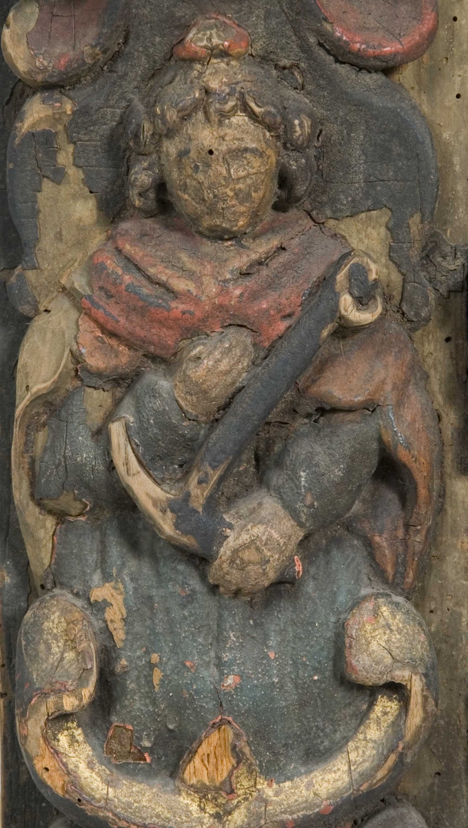 Skap med to dører. Skåret dekor, tre firgurer, en med slange i hendene, en med hendene i bedeposisjon, en med anker – representerer trolig hhv. visdom, tro og håp og visdom (tre av de syv dyder).