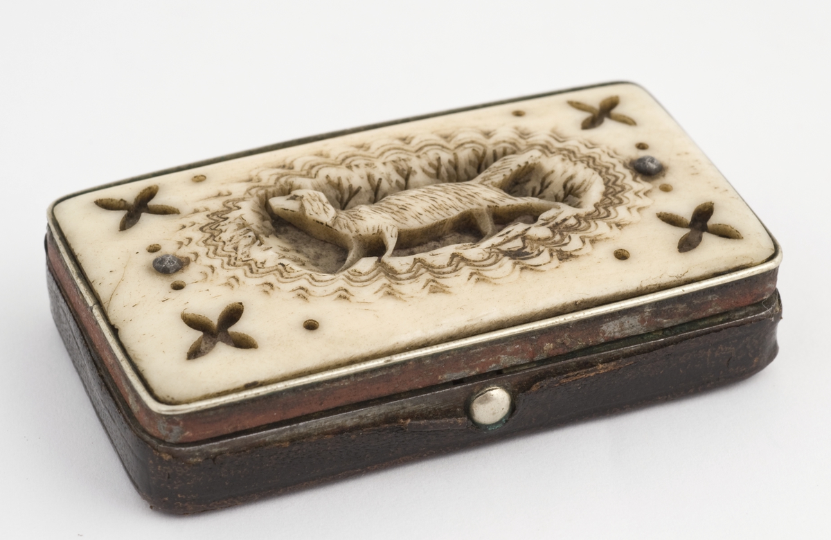 Snusdåse, stål trukket med skinn, lokk utskåret ben, hund i midten. Muligens 1840-årene fra Sørfondens samling.