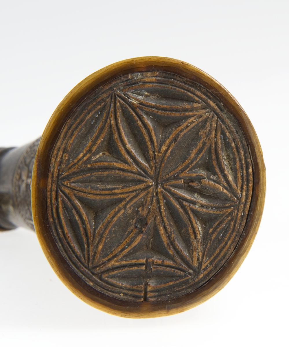 Krutthorn med flat, ornamentert bunnplate i tre. Ornamentikk på horn i form av 11 stk motivfelter omgitt av bårder med tekst. Motivene er: Adam og Eva ved Kunnskapens tre, Samson og løven, Daniel og dragen. Avbildede som rytterfigurer: Angolan, Karvel, Vidrik, Tidrik, Roland, Otvel, Burman og Olger Danske.
