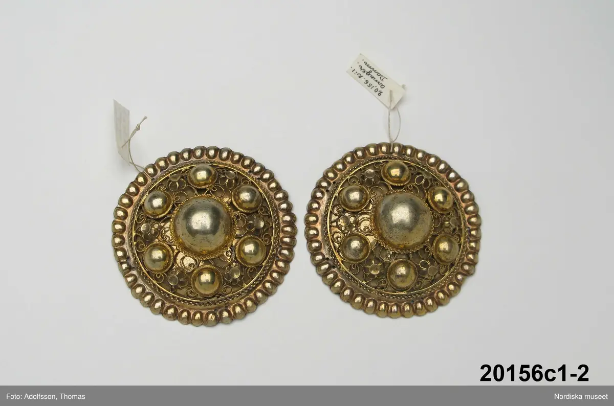 Huvudliggaren:
"Hollands draegt fr. Köpenhamn
Bestående af:
a) Kafetröje med Spaender [tillägg i blyerts.] skall vara kravetröje - 30 kr [spännet ommärkt till e+ 2011-03-08]
Spännet märkt: M.H.P.D.
b) Skjört - 28 kr
c) Forklaede med spaender - 30 kr
d) Haette med tillbehör och Haandstycke - 6 kr
e+) [spännet ommärkt till e+ 2011-03-08] Spännet märkt: M.H.P.D.
Ink. ss 20.087 [=ink. hos fru m. Wildschiödz i Köph. ss 20.001 [= gm (genom) dr A. Hazelius i Stockholm.]]- 94 kr. Under hösten 1877."
