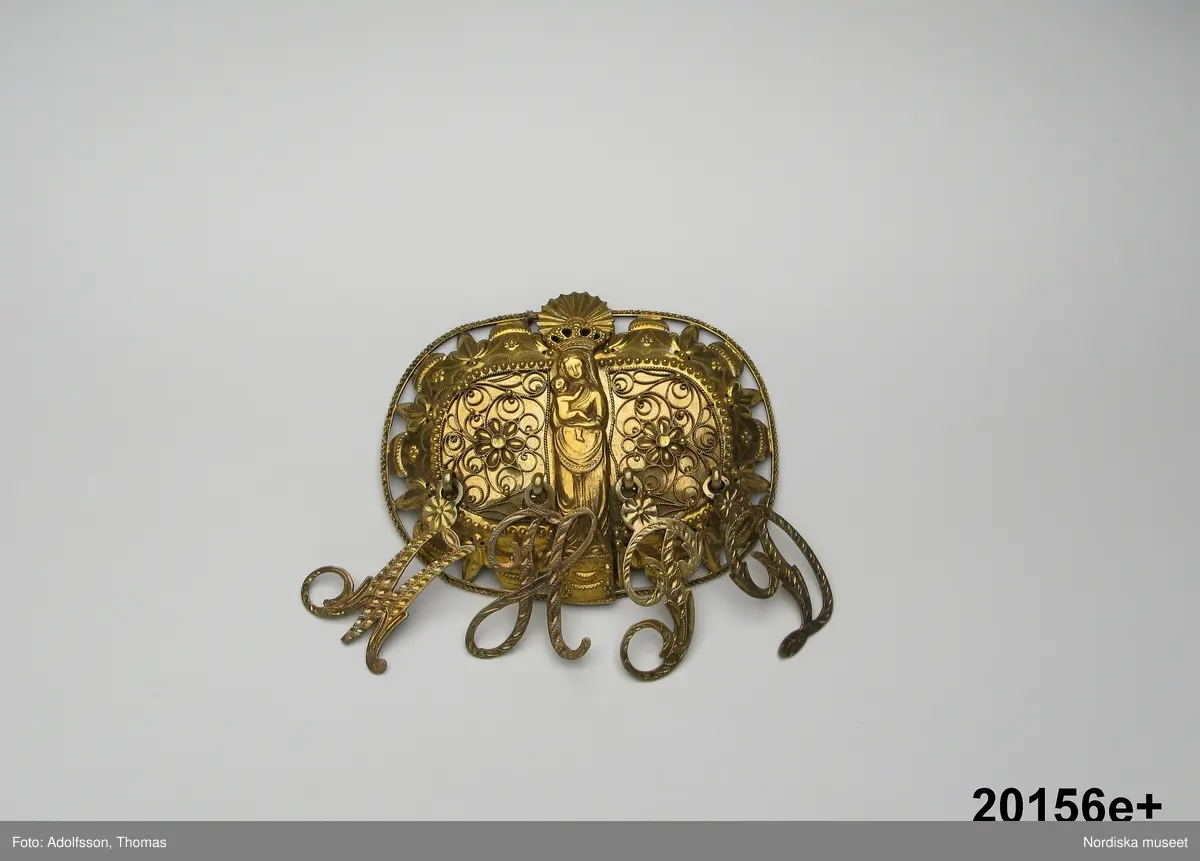 Huvudliggaren:
"Hollands draegt fr. Köpenhamn
Bestående af:
a) Kafetröje med Spaender [tillägg i blyerts.] skall vara kravetröje - 30 kr [spännet ommärkt till e+ 2011-03-08]
Spännet märkt: M.H.P.D.
b) Skjört - 28 kr
c) Forklaede med spaender - 30 kr
d) Haette med tillbehör och Haandstycke - 6 kr
e+) [spännet ommärkt till e+ 2011-03-08] Spännet märkt: M.H.P.D.
Ink. ss 20.087 [=ink. hos fru m. Wildschiödz i Köph. ss 20.001 [= gm (genom) dr A. Hazelius i Stockholm.]]- 94 kr. Under hösten 1877."
