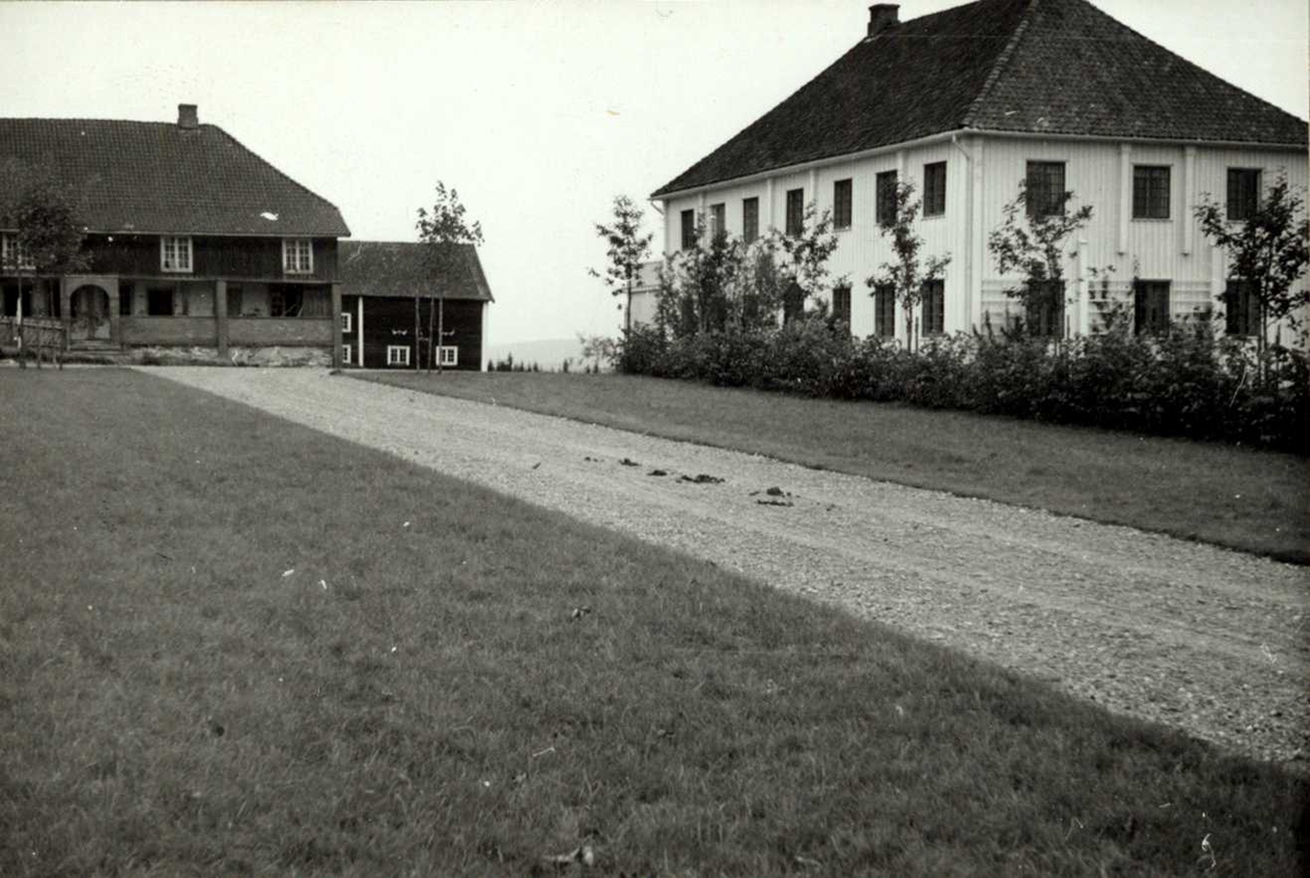 Opsett, Grue, Hedmark. Hvitmalt hovedbygning, mørk bygning med svalgang, uthus og vei.