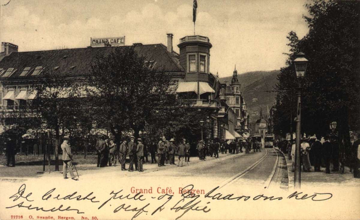 Postkort. Jule- og nyttårshilsen. Fotografisk motiv. Svart/hvitt. Fra gate i Bergen sentrum. Fotgjengere. Trikker. Stemplet 21.12.1908.