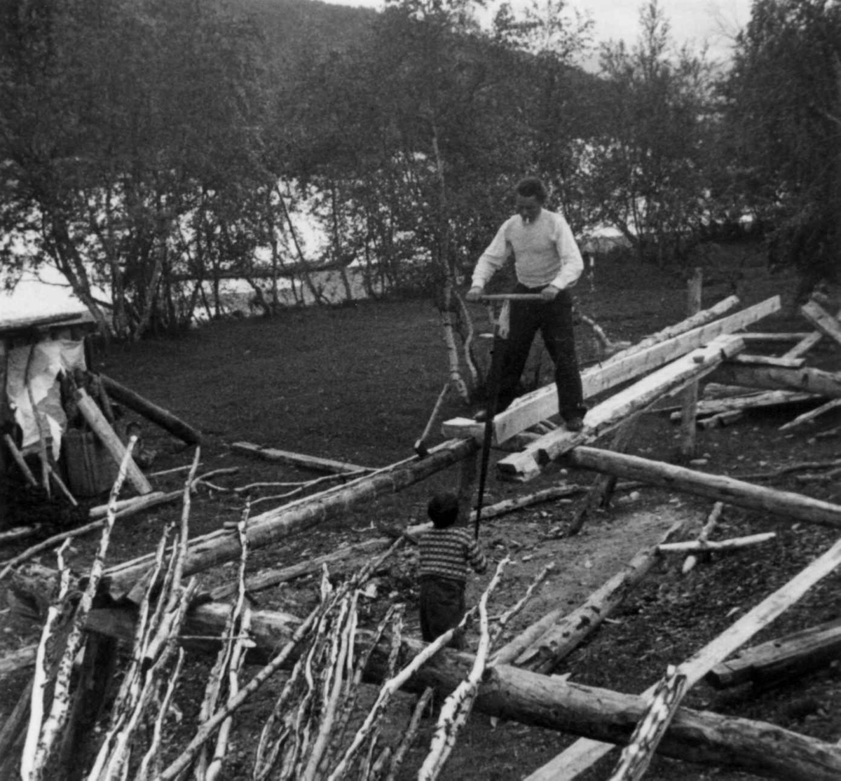 Alfred Rasmus Port bygger båt (1). En liten gutt holder i nederste enden av saga. Karasjok 1952.