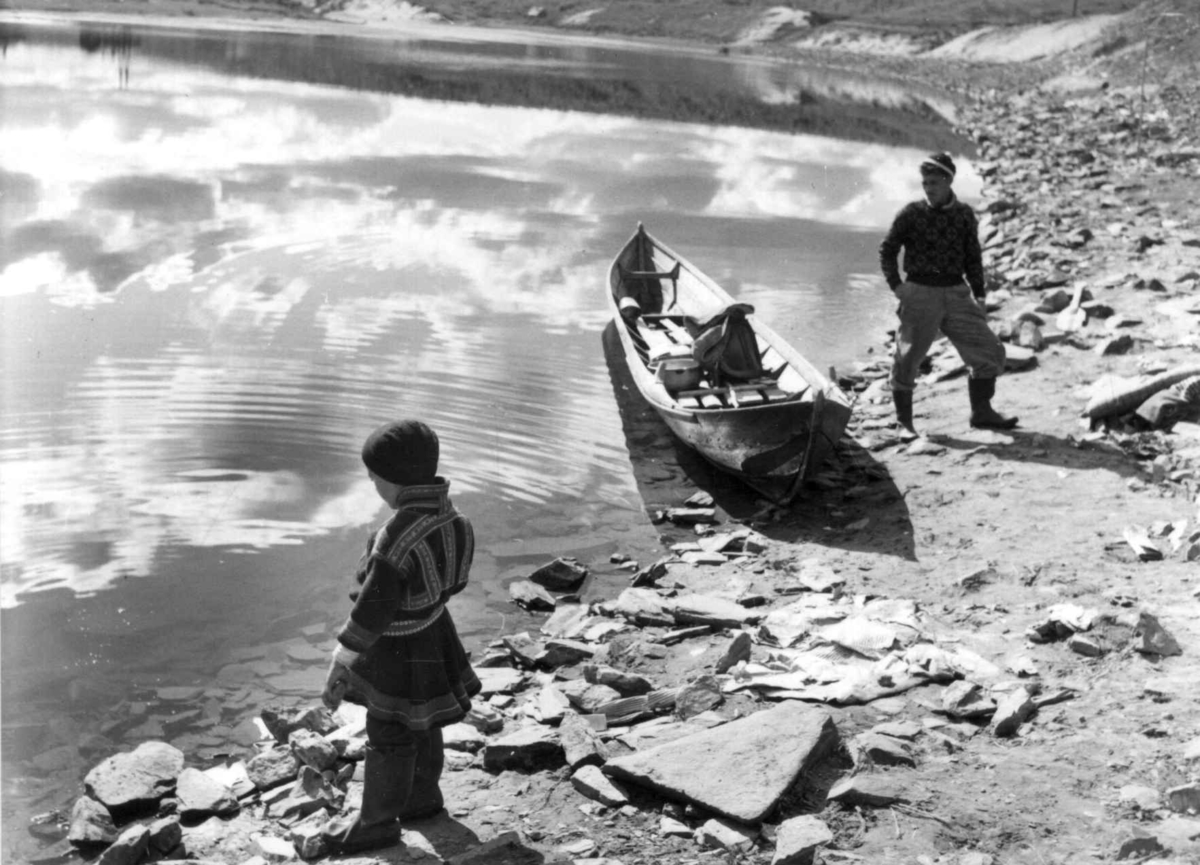 To personer og en liten båt ved elvebredden i Kautokeino 1956.