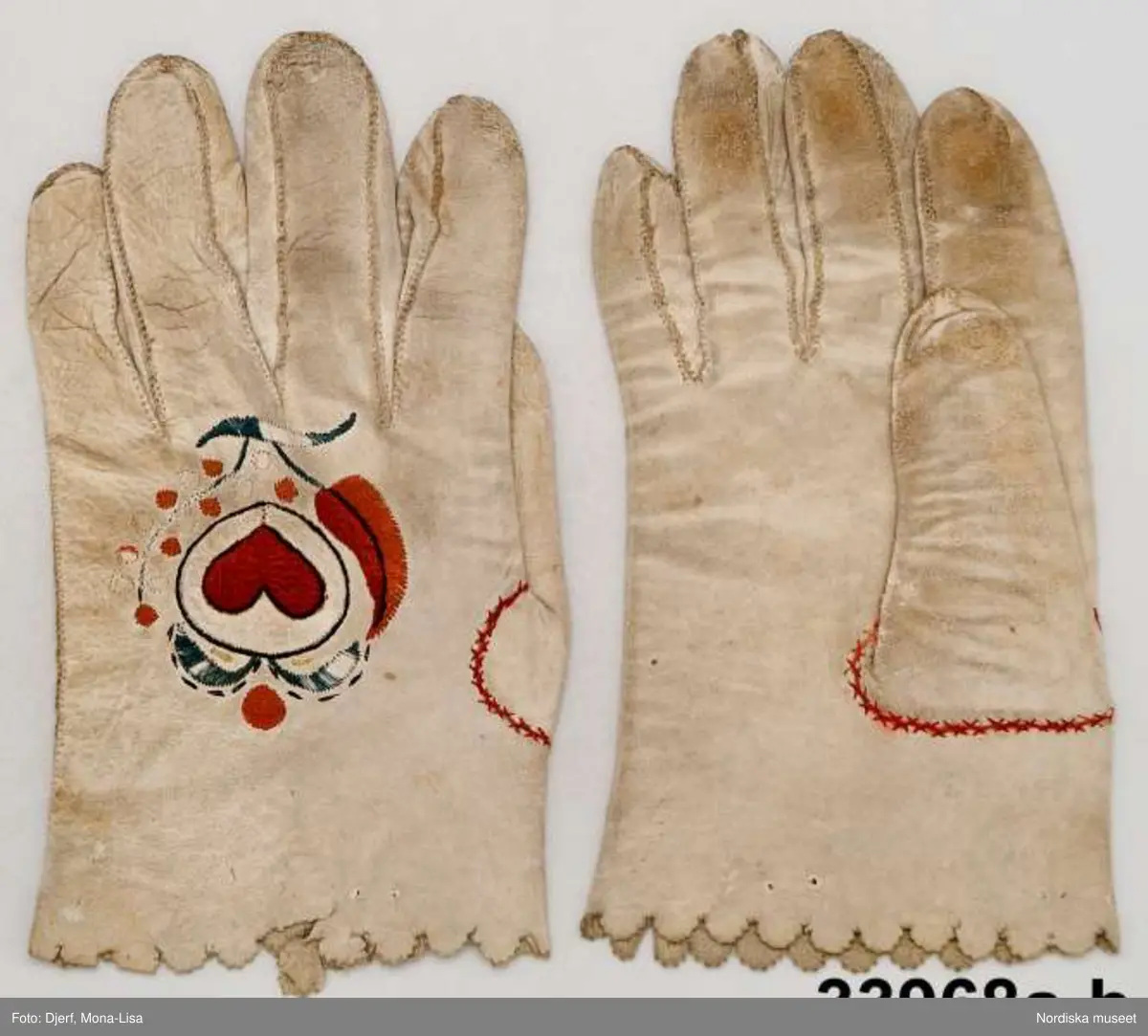 1 par handskar av vitt skinn med stansad uddkant på kragen. På handens ovansida silkebroderi i platttsöm och stjälksöm i mörkrött, grönt,  och svart,ett hjärta inskrivet i en cirkel och enkla blommor
Sådana silkebroderade handskar ingick i de standardgåvor som fästmannen gav sin blivande brud.
/Berit Eldvik 2013-02-28