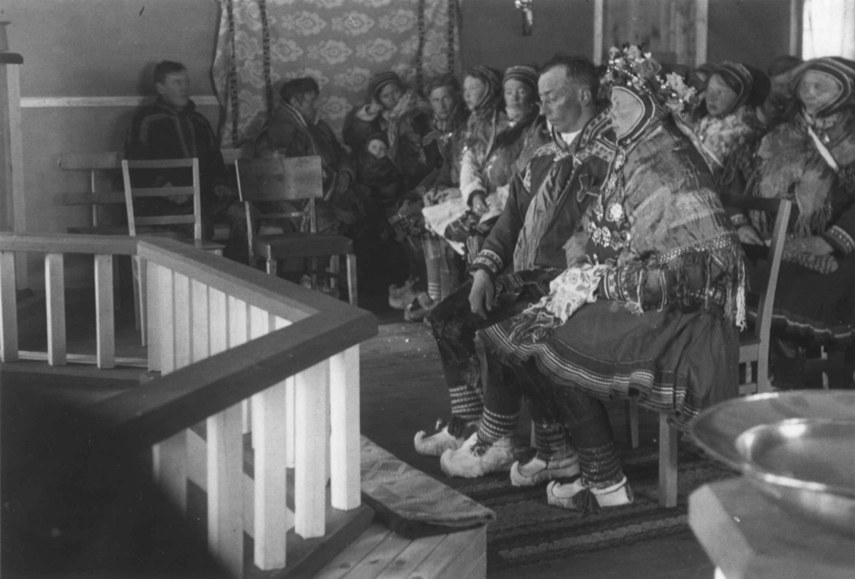 Bryllup i Kautokeino kirke, brudeparet sitter på hver sin stol foran alterringen. Mange personer tilstede.
