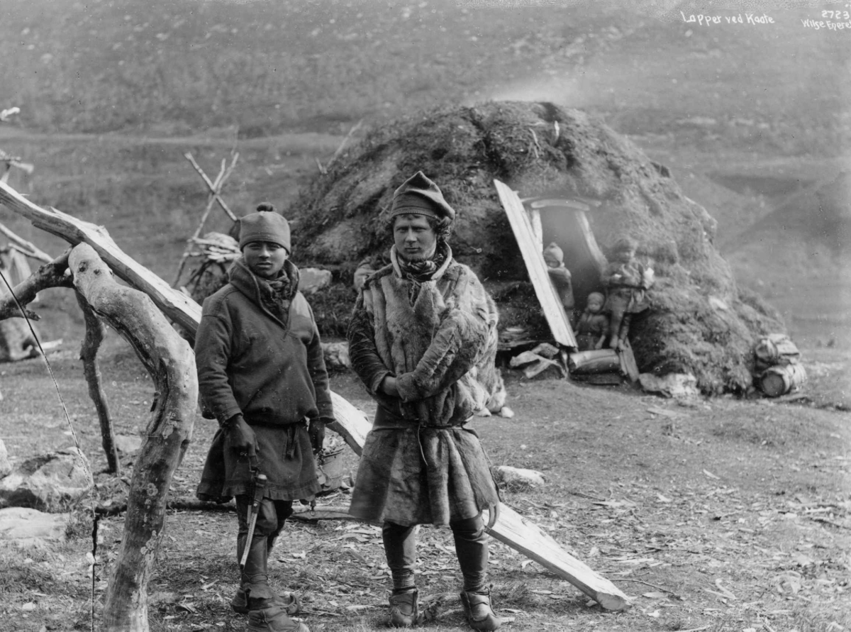 To svenske samer fra Karesuando foran en gamme, tre barn i døråpningen. Antagelig Tromsdalen ca. 1885-1892.