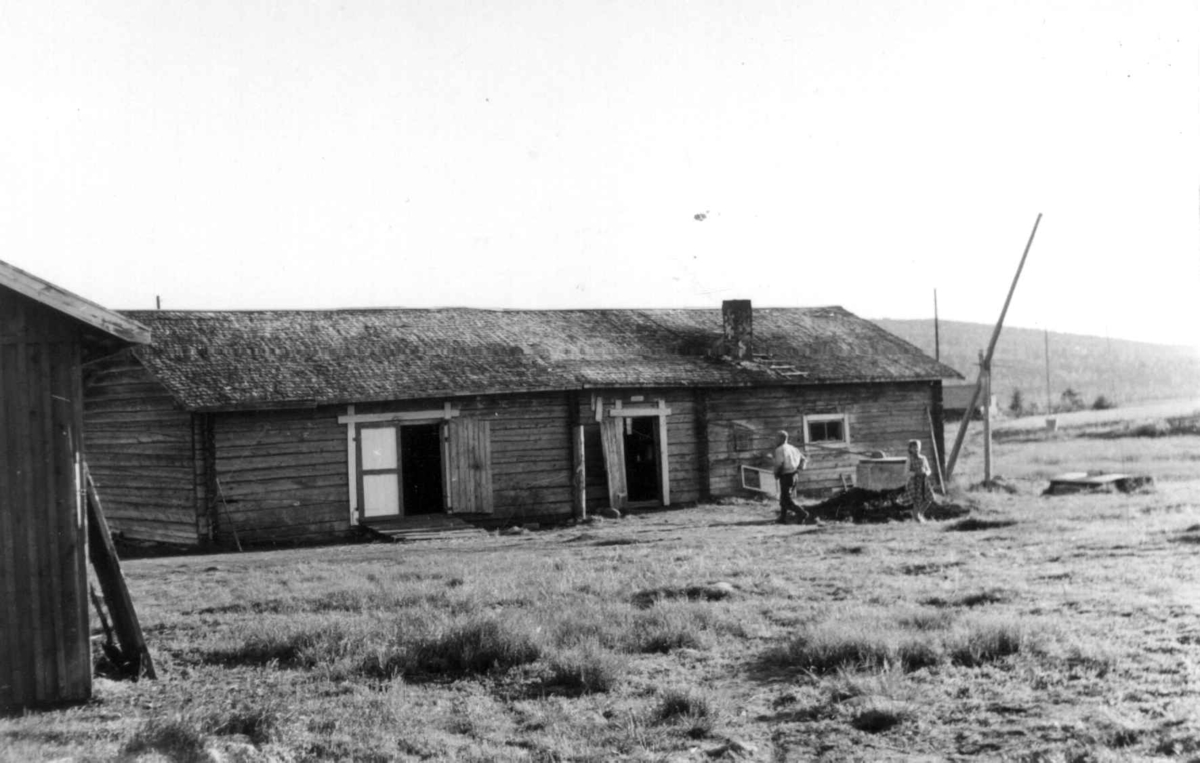 En fjøsbygning med en brønn ved siden av, to personer på gårdstunet. Aapua 1958.