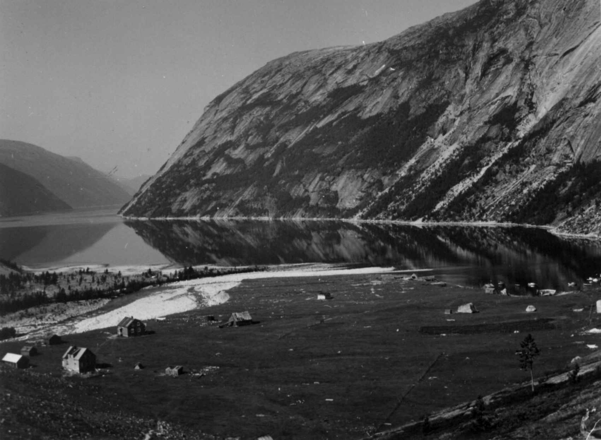 Oversiktsbilde over Hellemobotn med bebyggelse, 1964. Mareno Mikkelsen, født 1947, fra Vuodnabáhta / Hellemobotn forteller at bygningene er fra venstre; Fjøsen til Anders og Karen Urheim, hytta til Peder Mikkelsen, huset til Sigrid og Anders Mikkelsen, fjøset til deres hus. Det andre huset tilhørte Sigrid og Anders Mikkelsen og nede på sletta hytta til Inga og Augun Karlsen.