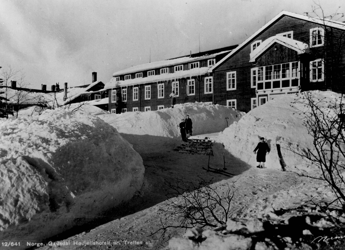 Avfotografert postkort. Fire personer i skitøy med ski og staver satt i snøen utenfor Gausdal høyfjellshotell.