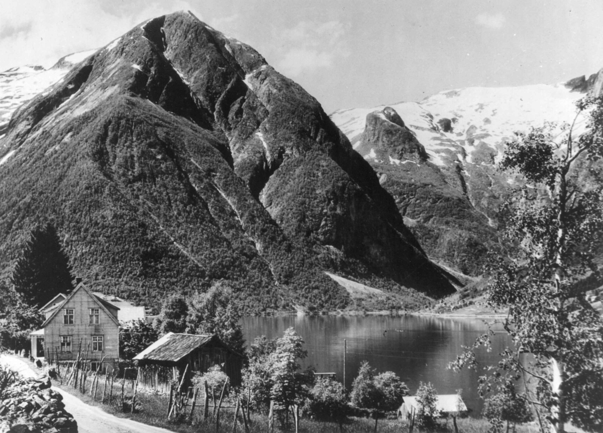 Utsikt over Esefjorden i Balestrand. I forgrunnen en liten gård, bak sees snødekte fjell.