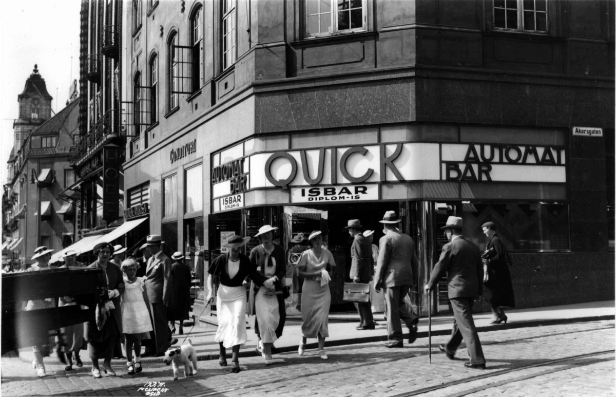 Hjørnet Karl Johans gate og Akersgata, Oslo 1935. Mennesker krysser gata foran Quick isbar.