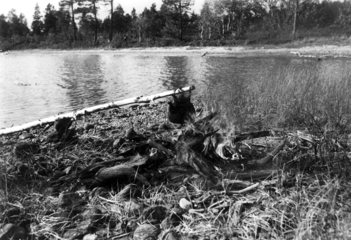 Kaffe-koking ved et vann, kaffekjelen henger på en stokk over bålet.. Mara Moja 14. august1959.