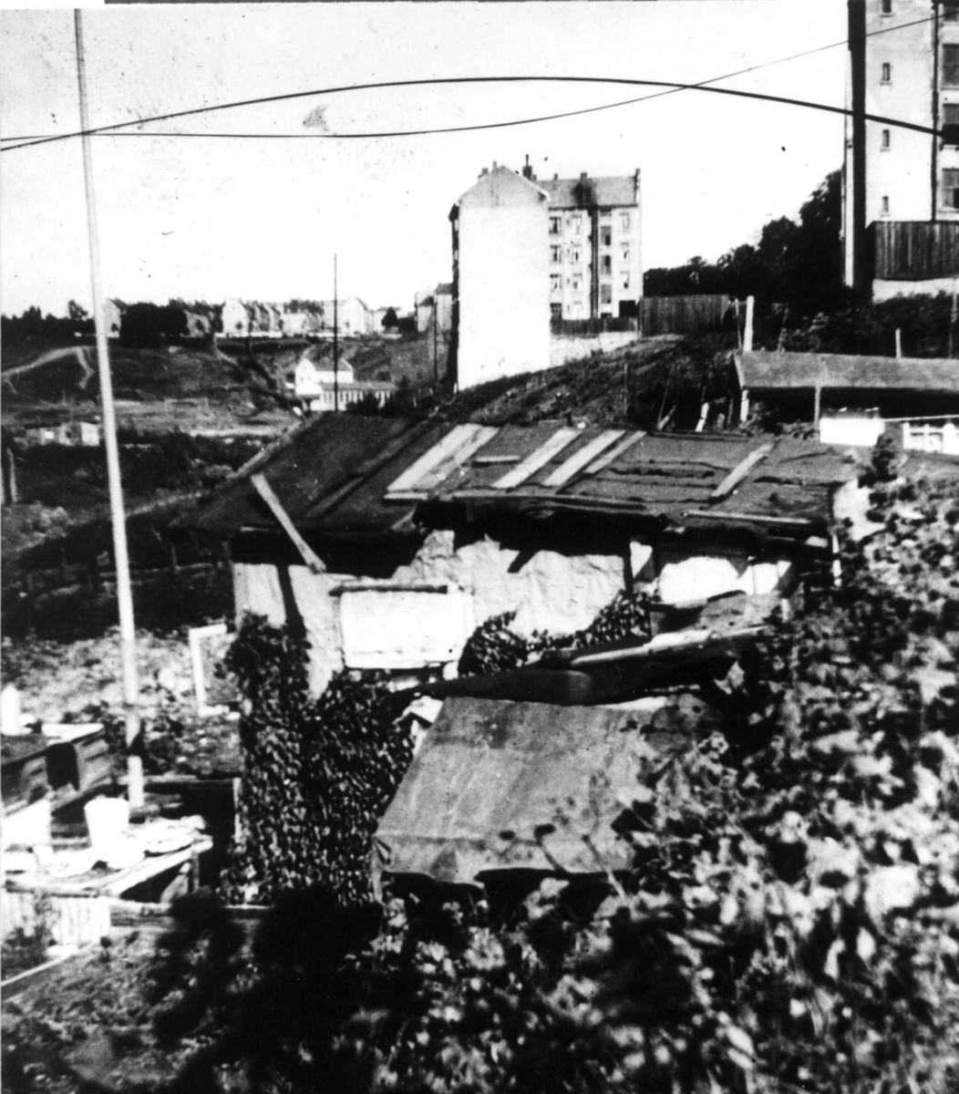 Hytter eller skur med murgårder i bakgrunnen, Oslo.
Fra boliginspektør Nanna Brochs boligundersøkelser i Oslo 1920-årene.