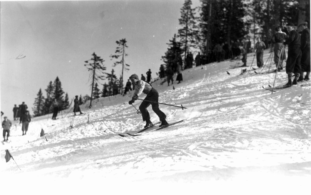 Slalåmrenn, Tryvannsåsen, Oslo 1934. En skiløper i fart ned løypa. Tilskuere på toppen av bakken.