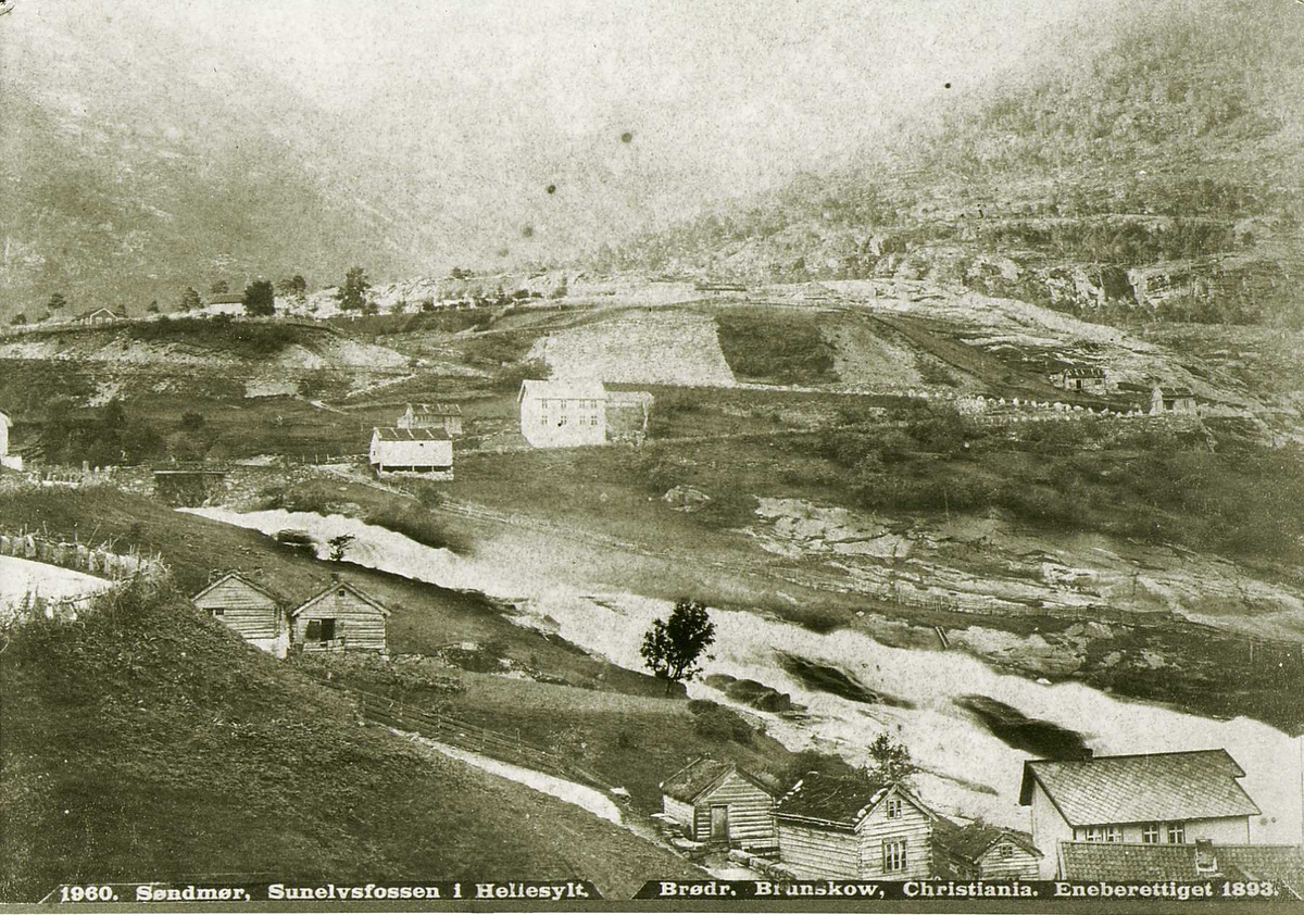 Utsyn over bebygd landskap i Hellesylt, Standa, Møre og Romsdal, med Sunnylvsfossen(?) Del av Brødrene Brunskows serie norske landskapsbilder.