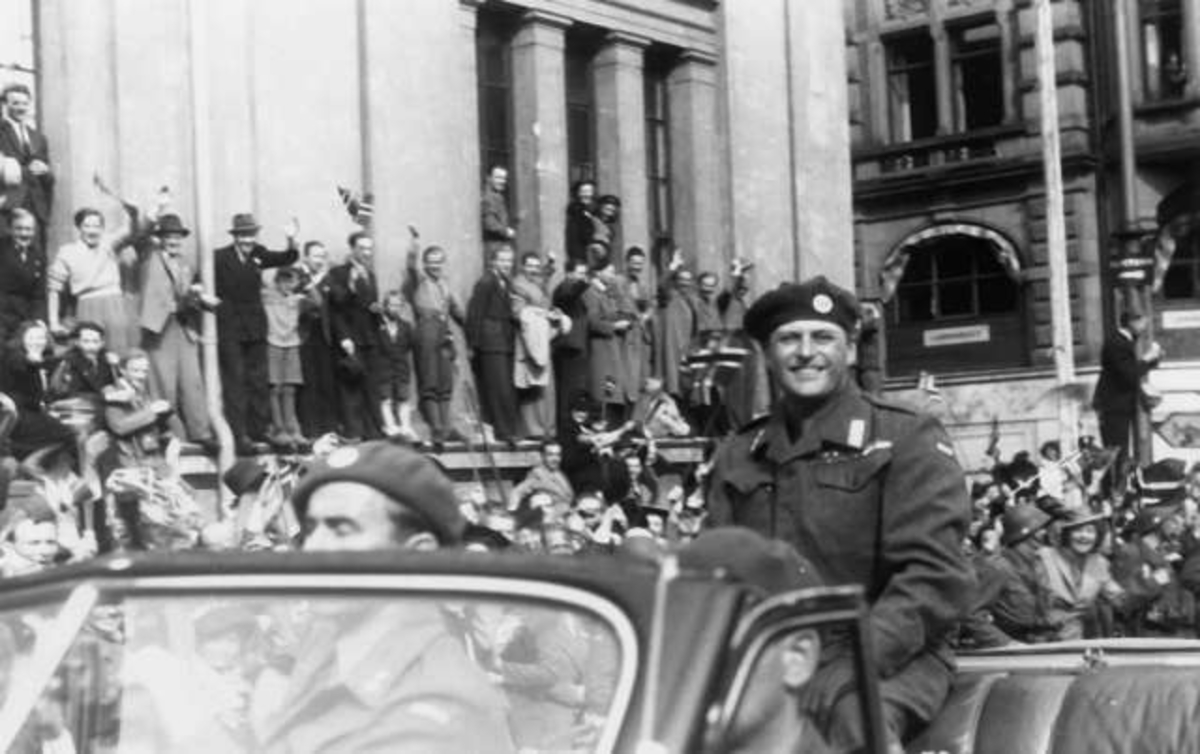 Fra Oslo under fredsdagene i 1945.
Den 13.mai kommer Kronprins Olav tilbake.Kortesjen kjører oppover Karl Johans gate i retning Slottet.Kronprinsen sitter på kalesjen og hilser til de fremmøtte.