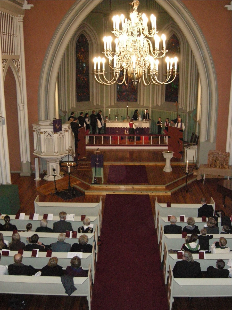 Første søndag i advent, åpning av kirkeåret. Sarpsborg kirke, Østfold, 02.12.2007. Prosesjon med kors, dåpsfølge på vei rundt alteret. I koret er dørene som er brukt i kirkeåpningsritualet åpnet. Alter, prekestol, døpefont, lysglober, kirkebenker, lesepult, lysekrone, julekrybbe og glassmalerier.