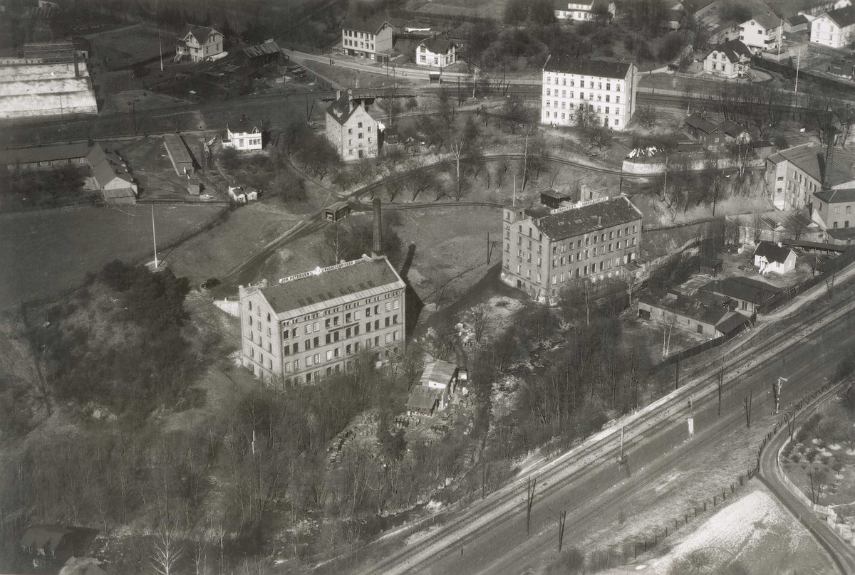 Bygninger ved A/S Joh. Petersens Linvarefabrik. Forstadsbane, jernbanespor og boliger. Gartneri i bakgrunnen.