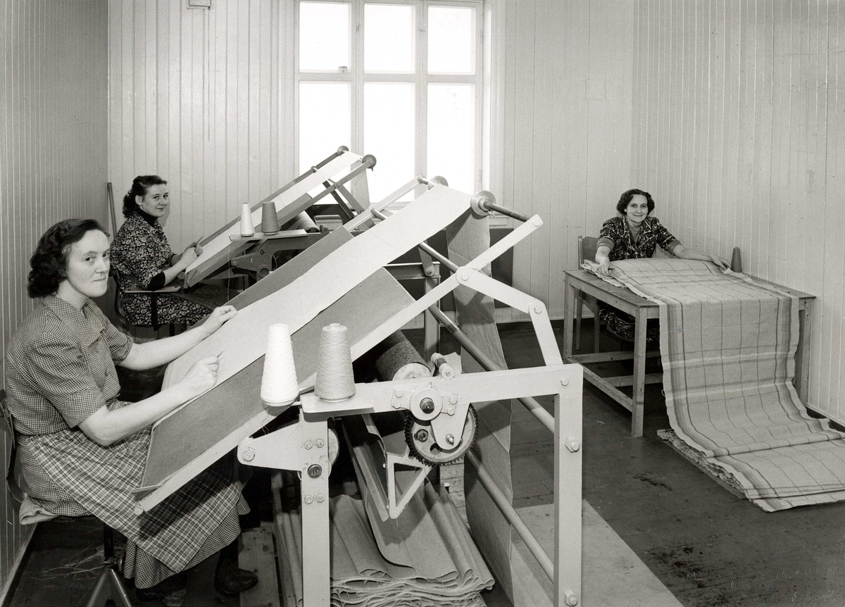 Tre kvinner arbeider med tekstil ved arbeidsbord på Gjøvik Veveri A/S.