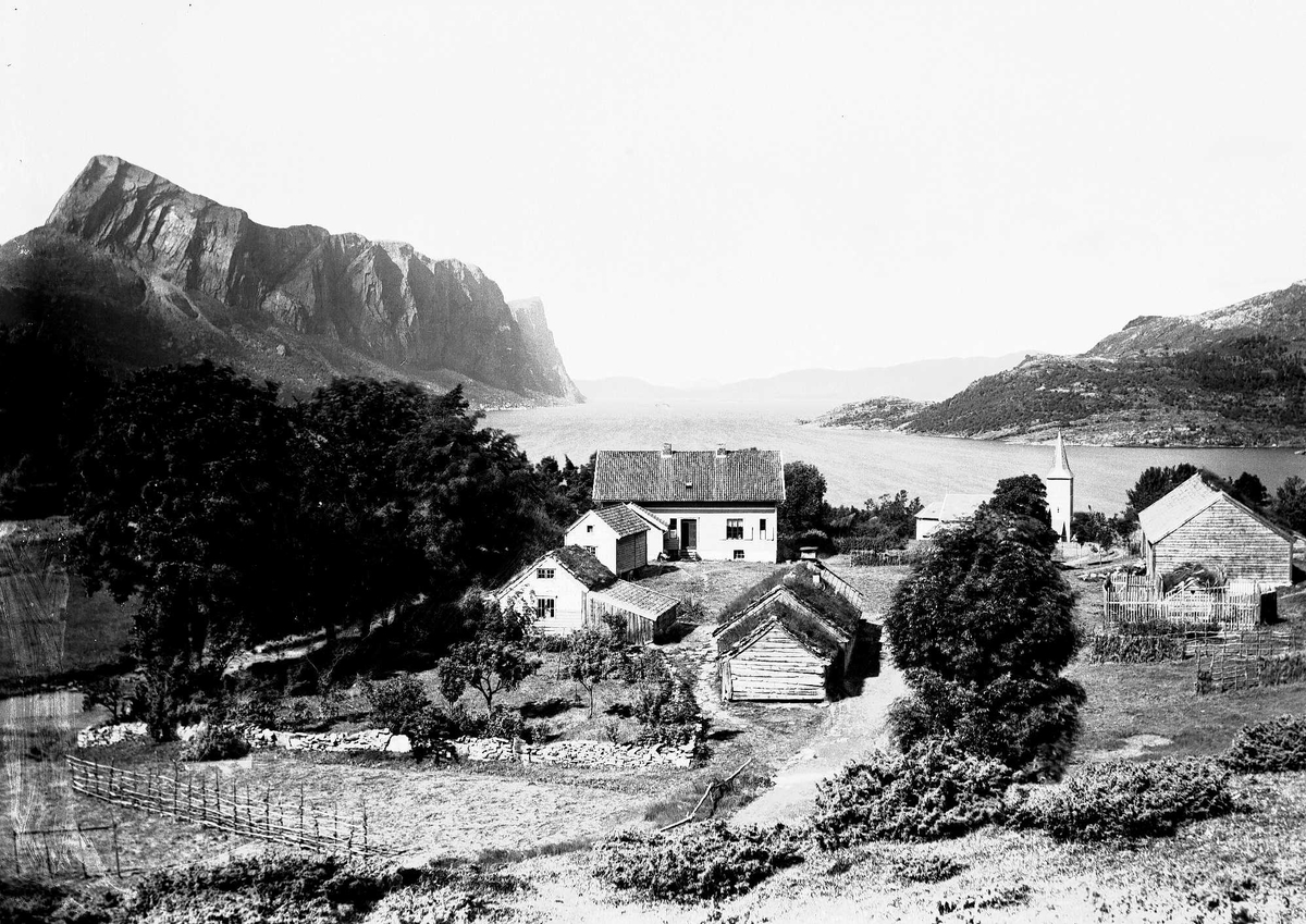 Fjell og fjord landskap med bebyggelse og trekirke. Antakelig Vestlandet.