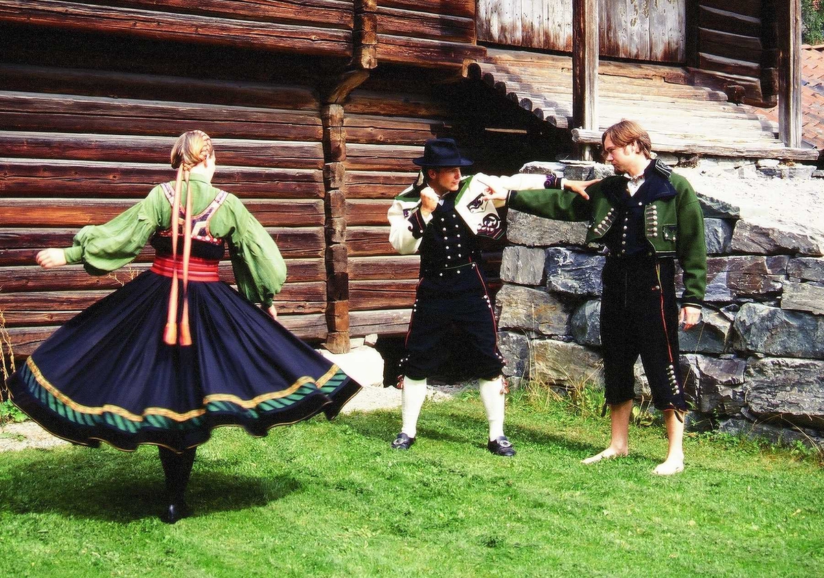 Verter i telemarksdrakter i Telemarkstunet foran Stalløa, bygning nr. 135 på Norsk Folkemuseum.