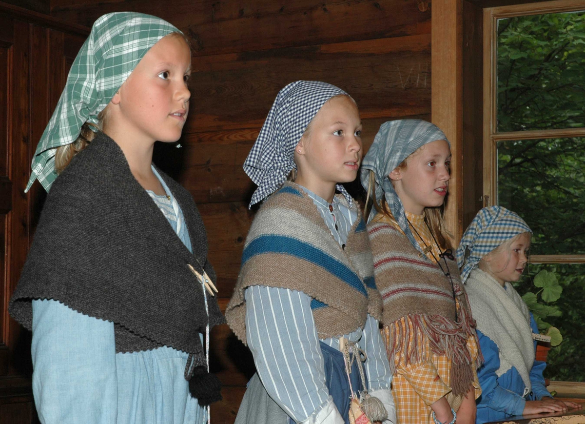 Levendegjøring på museum.
Ferieskolen uke 32 i 2005. Jenter i drakt følger undervisningen inne i Skolestua, bygning nummer 196 på Norsk Folkemuseum.