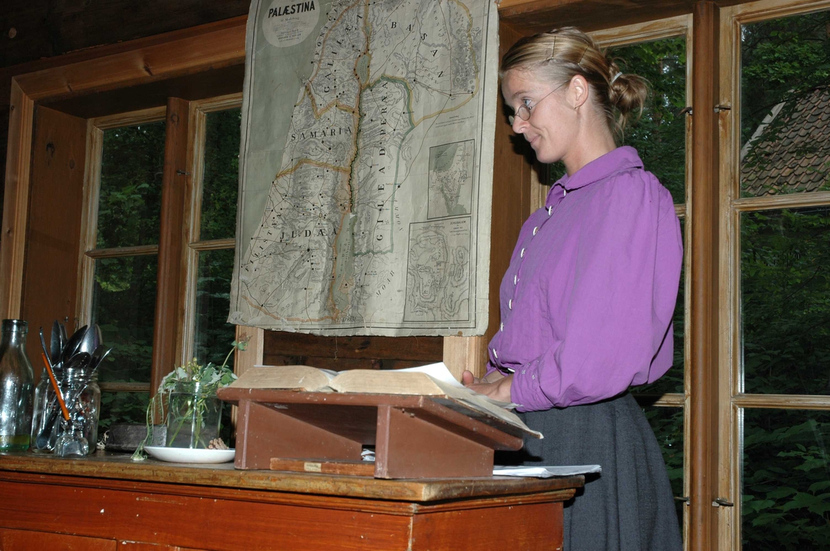 Levendegjøring på museum.
Ferieskolen uke 32 i 2005. Lærerinnen ved katereret inne i Skolestua, bygning nummer 196 på Norsk Folkemuseum.