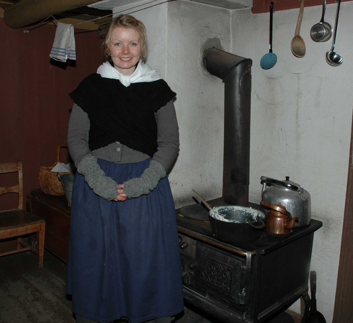 Kvinne i tidriktig kostyme foran vedkomfyren i et av husene på Enerhaugen i museets gamleby. Julemarked 27.11.2005.