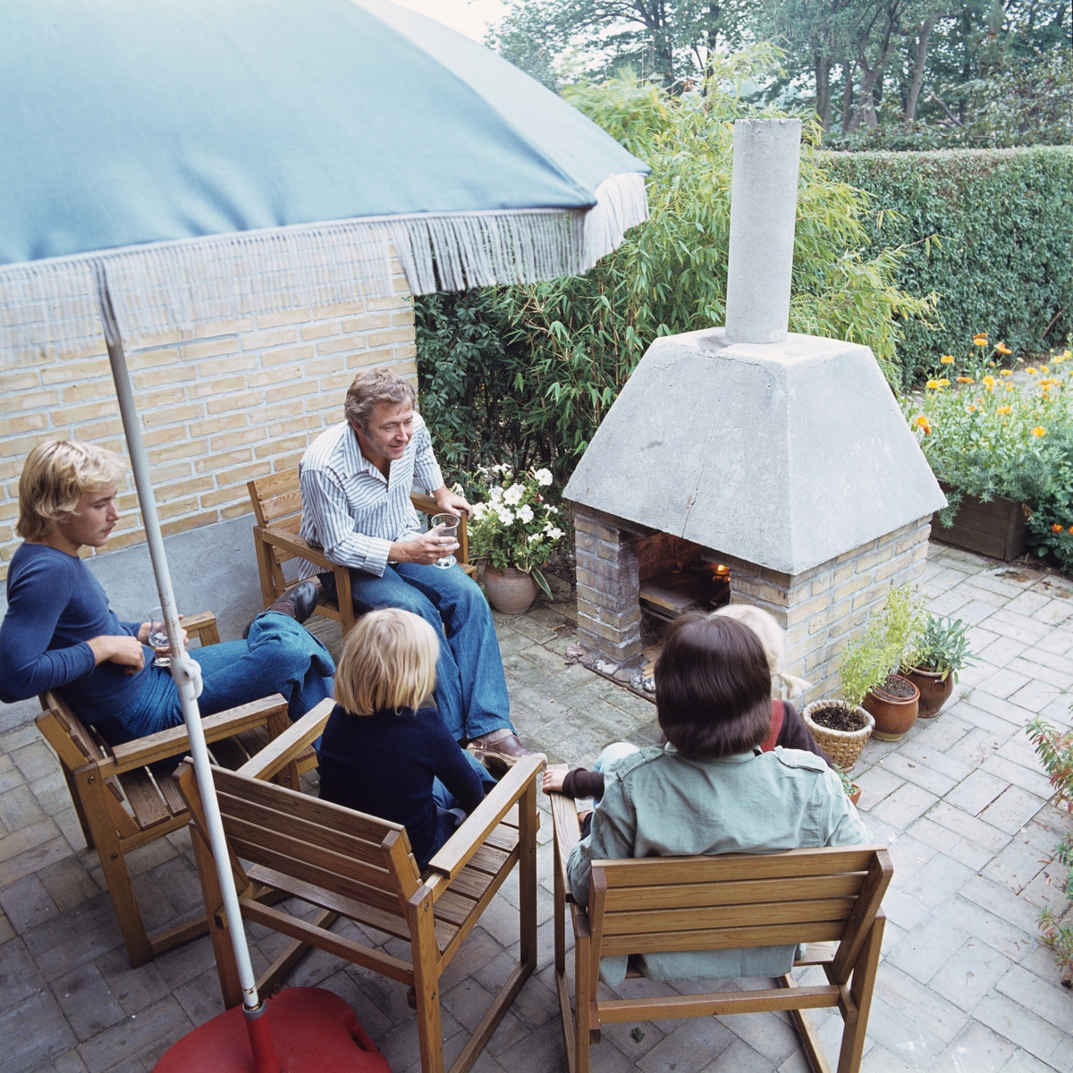 En familie sitter på terrassen ved en utepeis. Illustrasjonbilde fra Bonytt 1986.