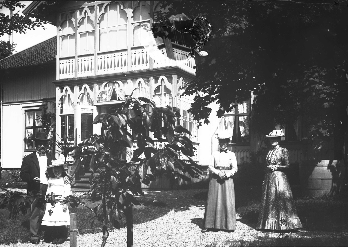 Familieportrett, to kvinner, mann og en pike i hagen foran inngangsparti og veranda. Muligens Villa Grande, Drøbak, Frogn, Akershus. Ca 1900-1905.