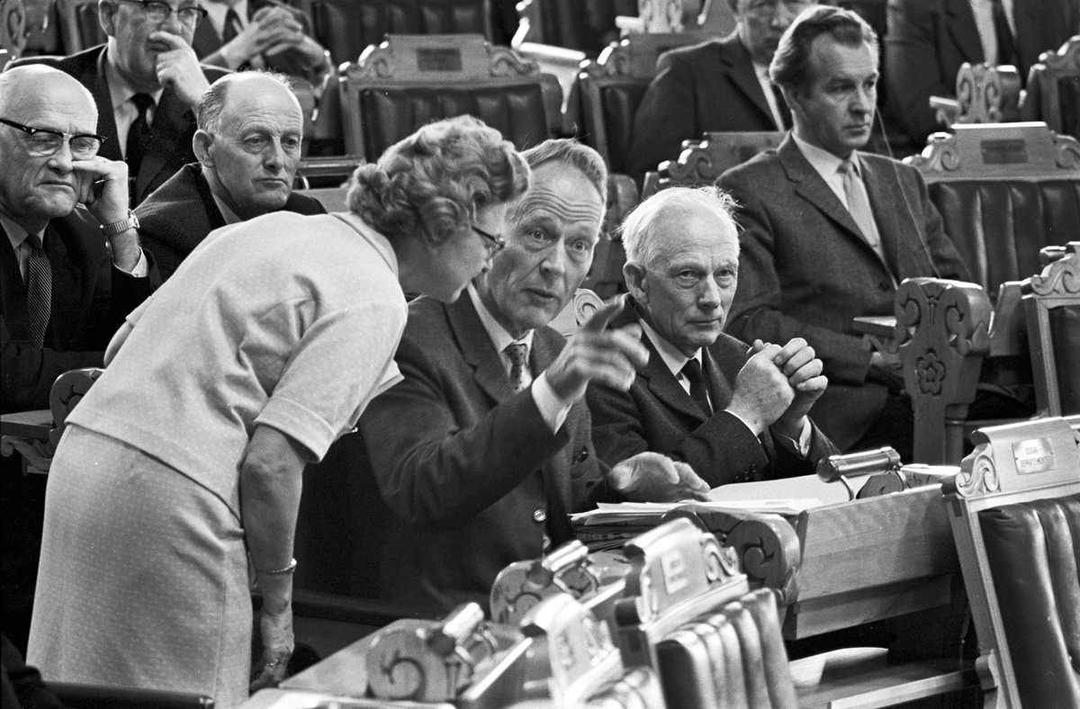 Serie. Debatt i Stortinget. Kåre Willoch og John Lyng leser dokumenter og en kvinne snakker med en politiker. Fotografert våren 1967.