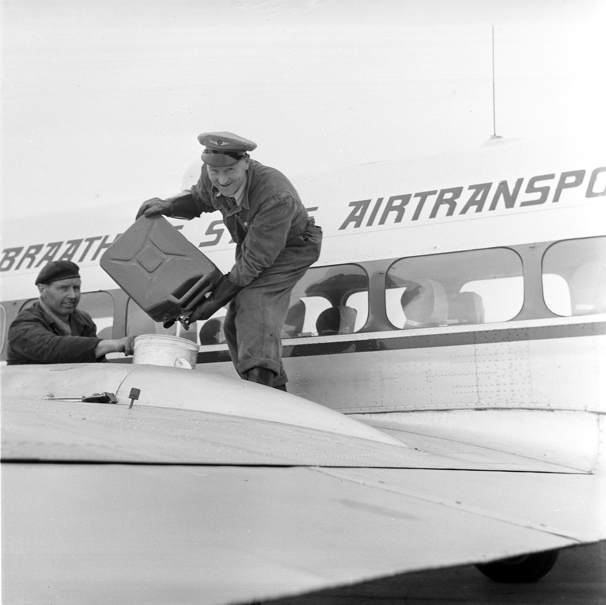 Serie. Før og under åpningen av Vigra flyplass. Mange arbeider rundt på området, noen menn står samlet og passasjerer går ombord på et Braathens safe fly. En dame står ved oppvaskbenken.  Fotografert juni 1958.