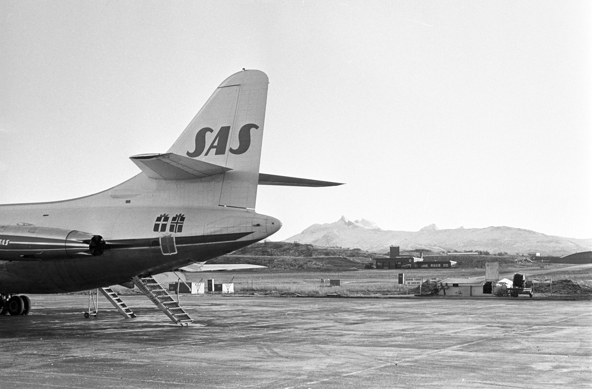 Serie. Ombord på SAS flyet til Tromsø. Flyfoto over snødekkete fjell. To flyvere i flytårnet. To menn og en kvinne, ant. Eva Lie, sitter rundt et bord. Fotografert desember 1965. 