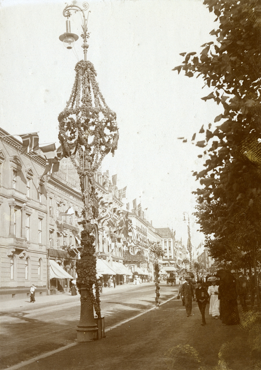 Serie med fire foto fra den franske prsidenten Clement Armand Fallières statsbesøk i Kristiania i 1908. Velkomstpaviljong med baldakin, pyntet med girlander og flagg. Dekorasjoner utført av B. Lange, antakelig. Tilskuere på Honnørbrygga i hovedstaden. Karl Johans gate er også pynytet med dekorasjoner.