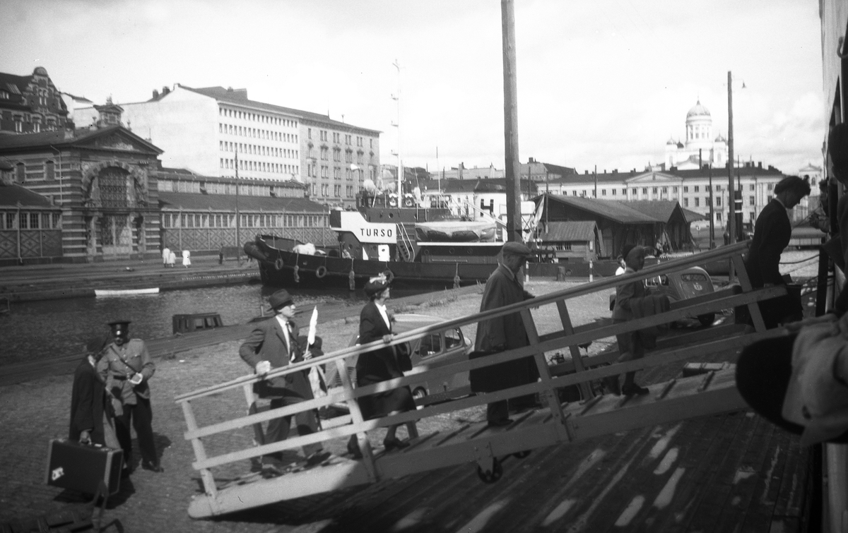 Passasjerer går om bord i ferge i havnen i Helsinki. Domkirken i bakgrunnen. Fotografert 1951.