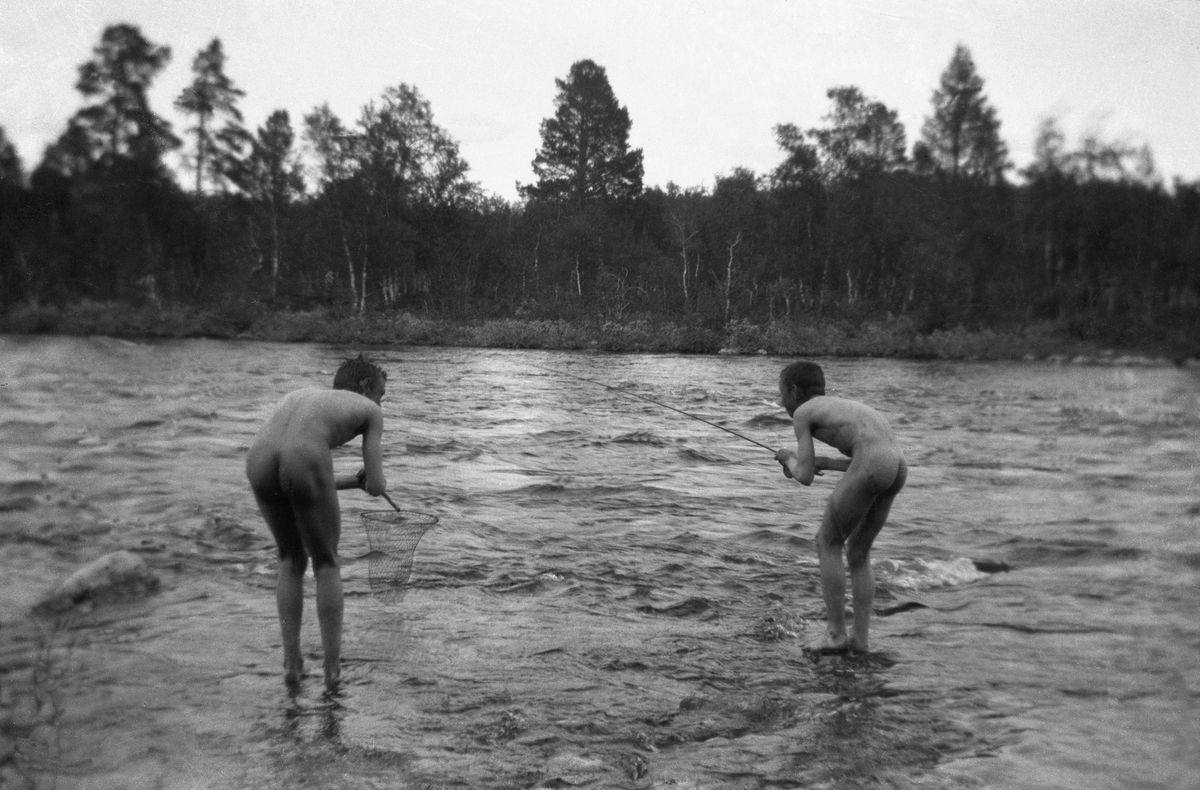 To gutter fra Arentz-familien står nakne i Glomma og fisker med stang og nett. Fotografert ca. 1912-13.