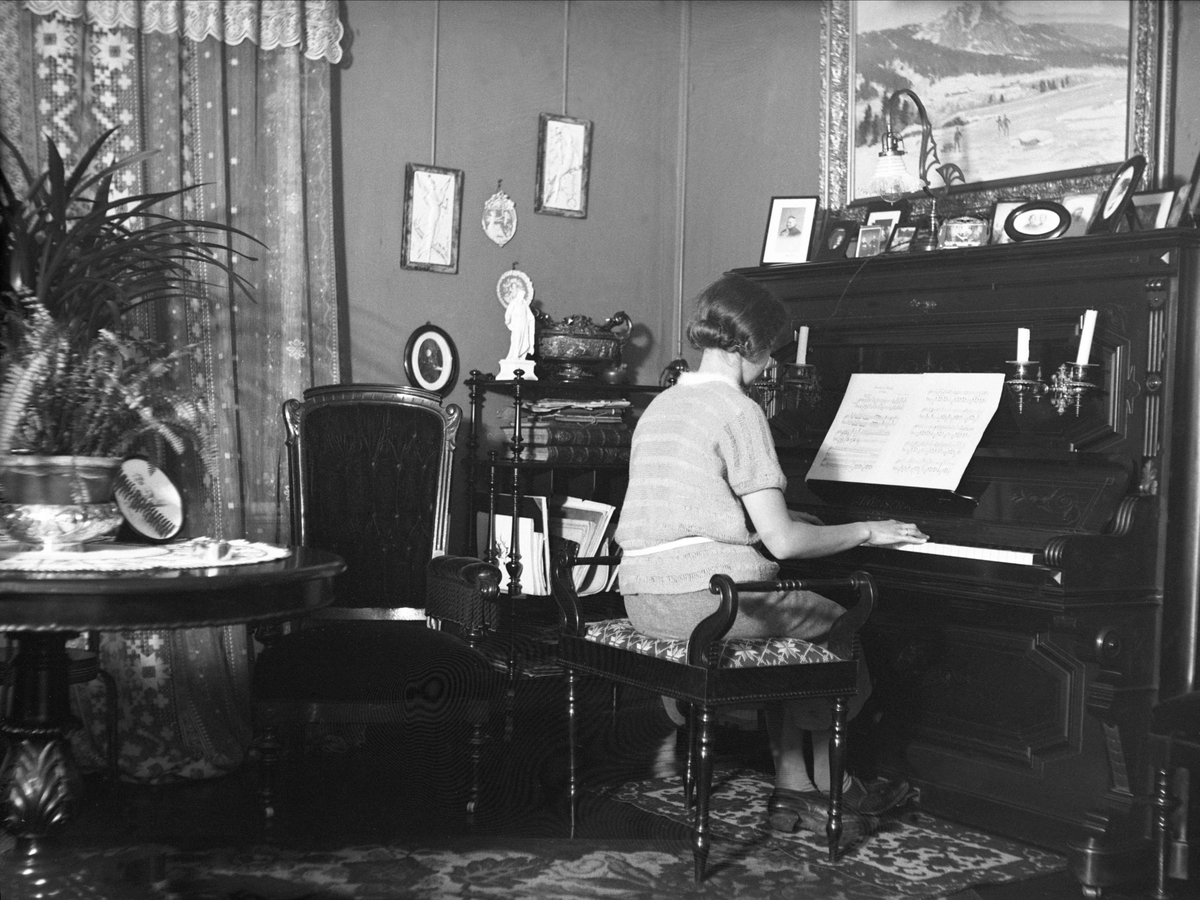 Dordi Arentz sitter i en stue og spiller piano, Fredrikstad. Fotografert januar 1926.