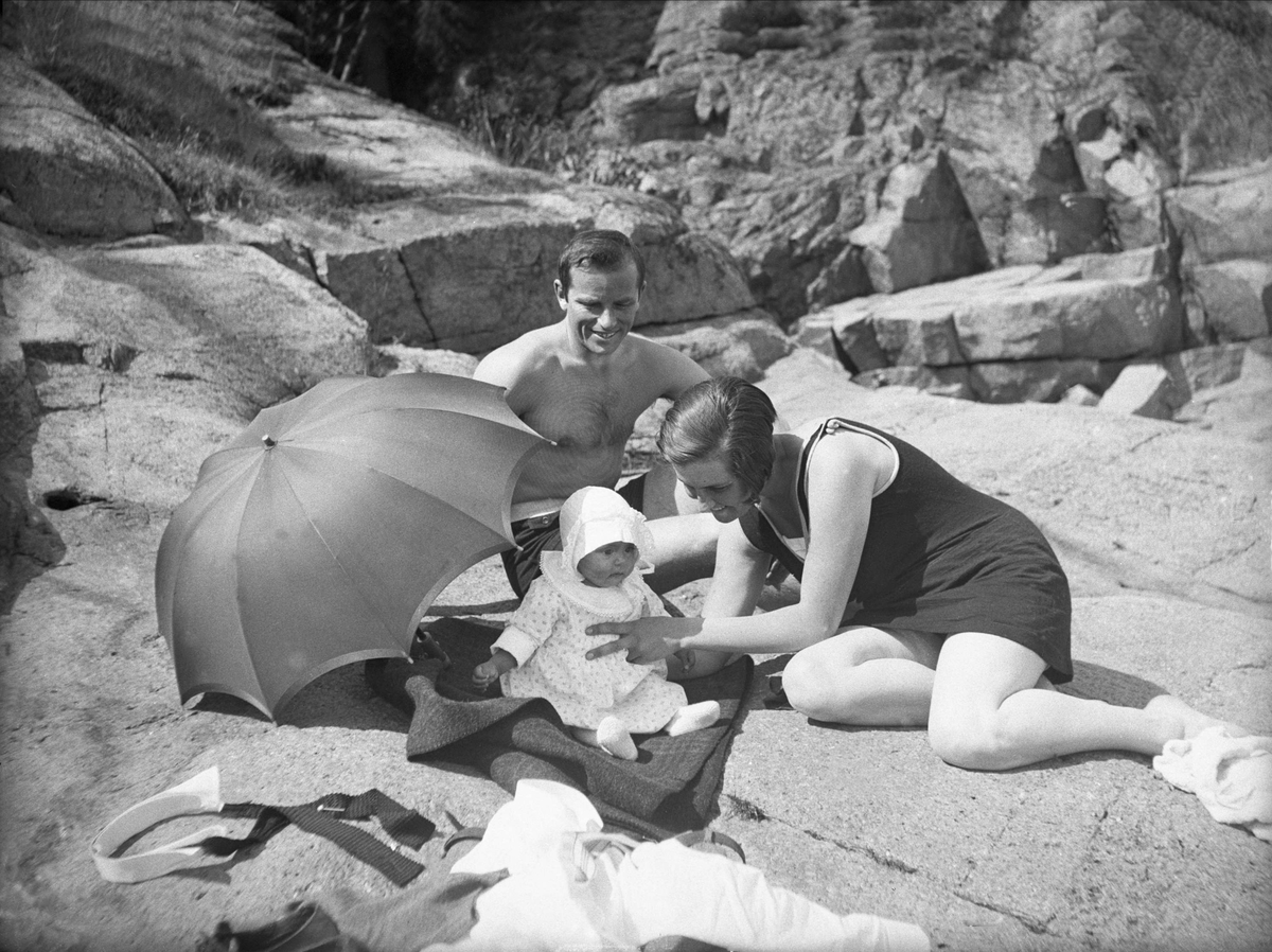 Dordi og Fritjof Arentz sitter sammen med deres datter Guri på badestranden. Fotografert juli 1929.