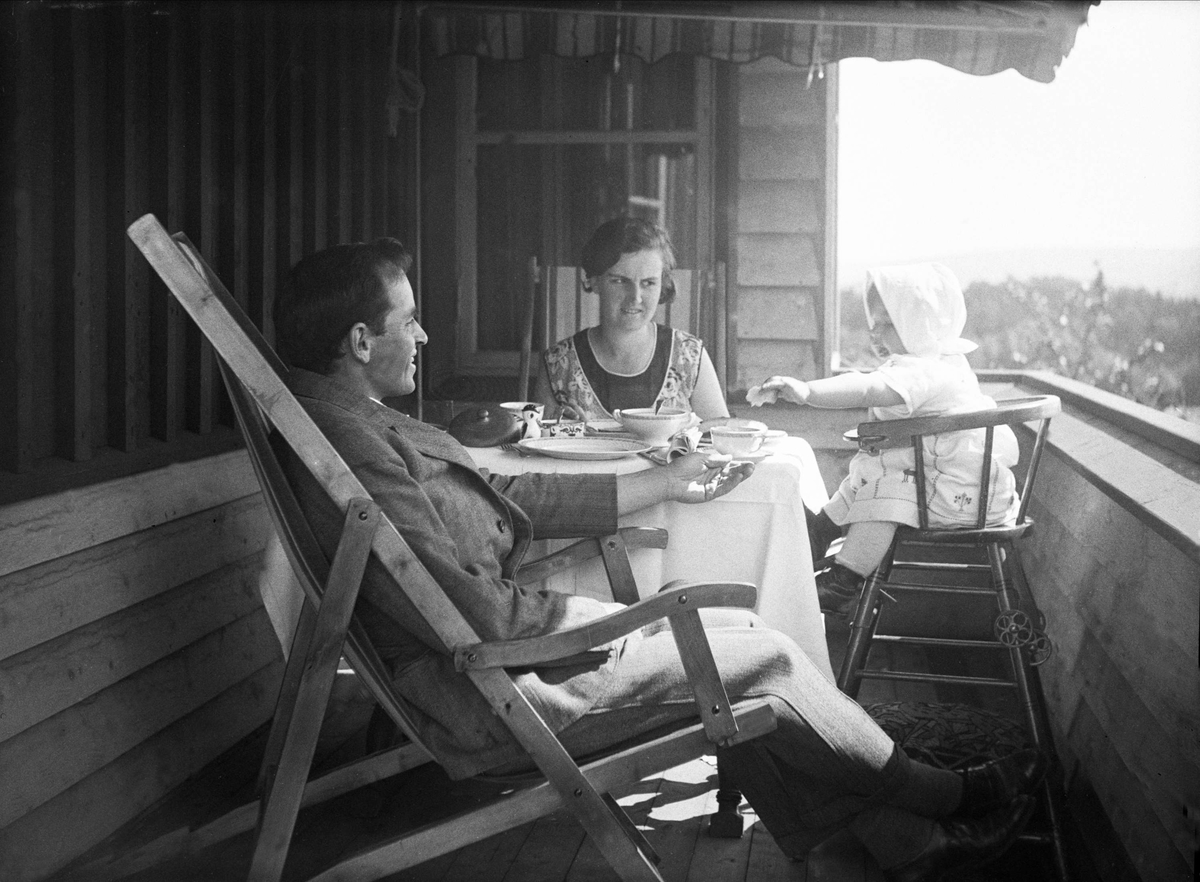 Dordi og Fritjof Arentz sitter på verandaen og spiser frokost sammen med deres datter Guri. Fotografert mai 1930.