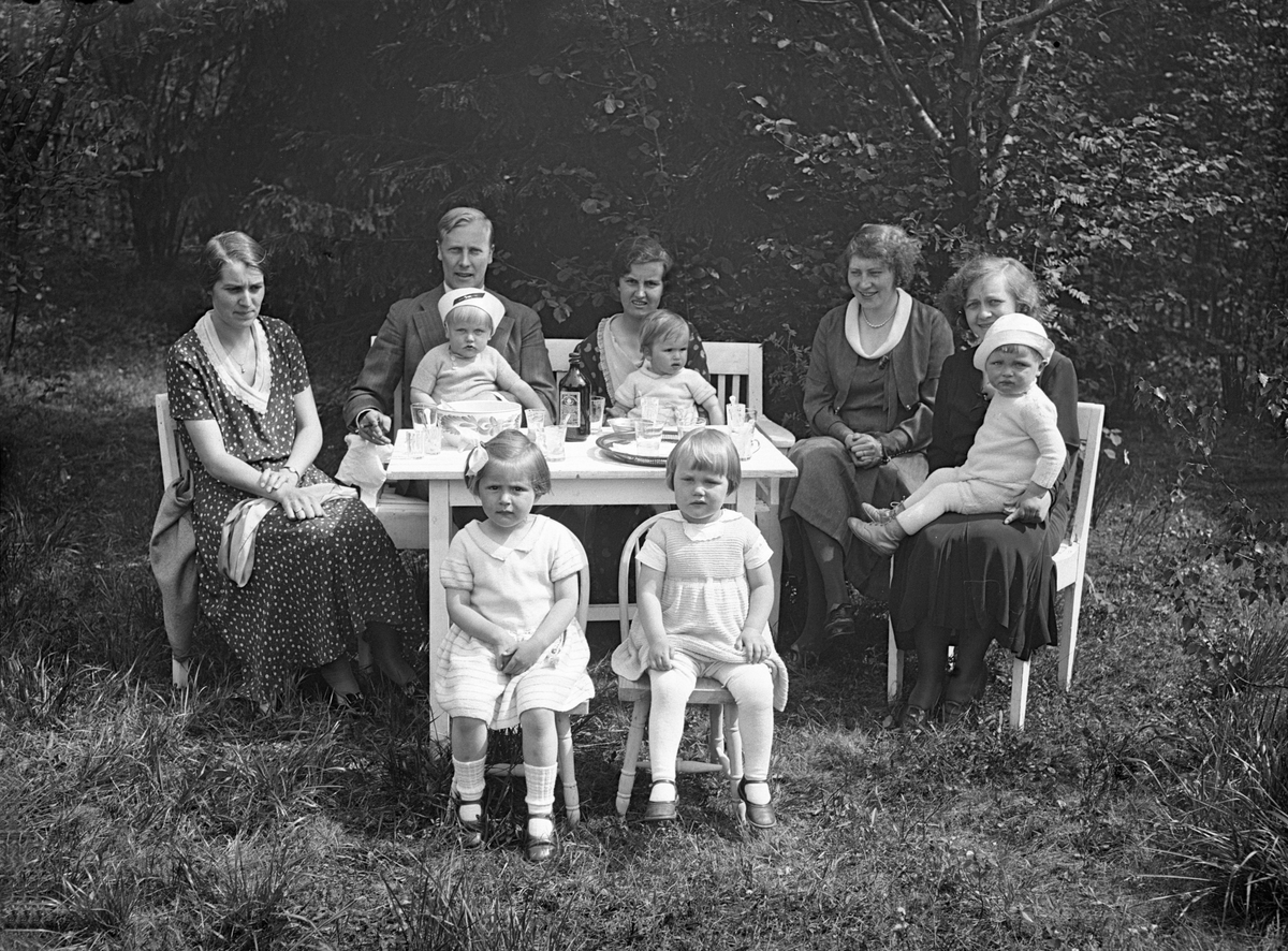 I hagen til familien Ramstad sitter Clara og Sverre Ramstad og deres barn Bengt og Bitten og Dordi Arentz med sine døtre Siri og Guri og to ukjente kvinner med et barn på fanget. Fotografert juni 1932.