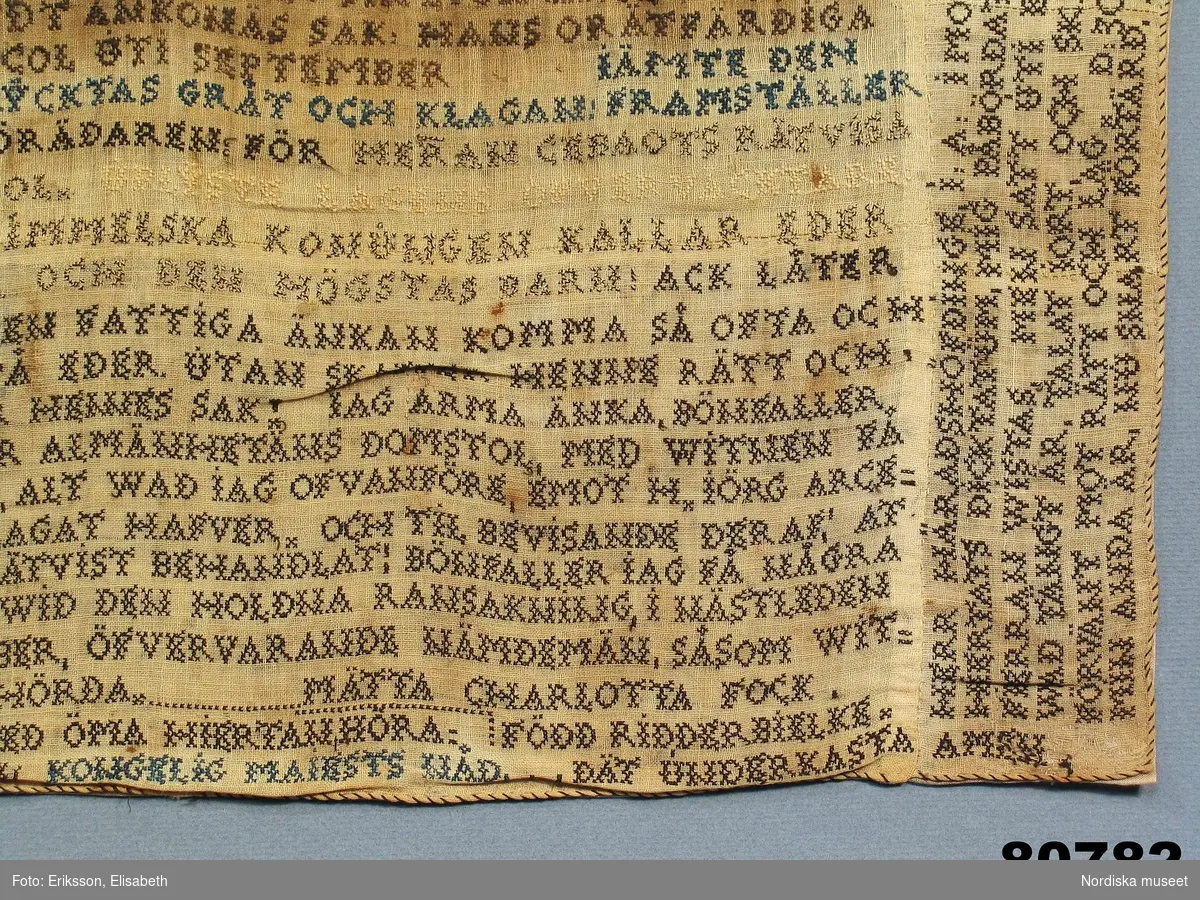 Lång text broderad i korssöm i svart, blått och vitt tunt lingarn på ofärgat tuskaftat linne, sammansytt av 27 små tygbitar. Väven har 25 tr/cm och 24 insl/cm. Rullfåll med svart tråd. Texten är en klagoskrift och en vädjan om nåd från Mätta Charlotta Fock f. Ridderbielke daterad Jönköpings bastil den 10 däsember 1805.
"Ridderbielke, Metta Charlotta, gift med sergeanten Henrik Johan Fock, förgjorde 1802 sin man jemte tvänne sina barn genom gift, för att få gifta sig med sin amant, gifte skogvaktaren, sedermera roteringskarlen, Johan Fägercrantz, sedan Lilja kallad, som dömdes till 28 dygns vatten och bröd. Efter flera års sittande på bekännelse å Carlstens fästning, blef hon slutligen dömd att mista högra handen, halshuggas och å båle brännas, hvilket allt försiggick d. 7 Nov, 1810 å Fägredsmon i Westergöthland."
Ur Anteckningar om svenska kvinnor utg. 1864 av P.G. Berg.
Hennes skuld kunde aldrig bevisas och klagoskriften är  en nådeansökan för den orättvisa rättegång och dom som hon menar sig ha fått. 
Hela texten i broderiet.  se under Information.
Anm. Broderiet urtaget ur sin glasade ram.
/Berit Eldvik 2011-12-29