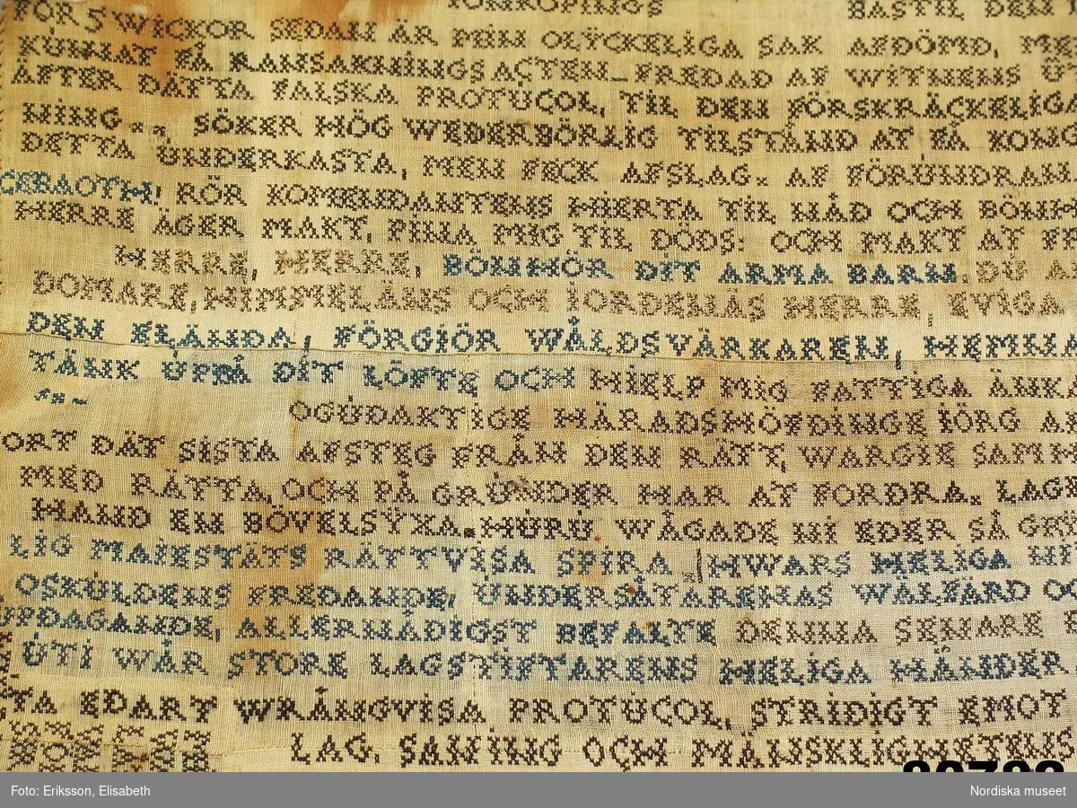 Lång text broderad i korssöm i svart, blått och vitt tunt lingarn på ofärgat tuskaftat linne, sammansytt av 27 små tygbitar. Väven har 25 tr/cm och 24 insl/cm. Rullfåll med svart tråd. Texten är en klagoskrift och en vädjan om nåd från Mätta Charlotta Fock f. Ridderbielke daterad Jönköpings bastil den 10 däsember 1805.
"Ridderbielke, Metta Charlotta, gift med sergeanten Henrik Johan Fock, förgjorde 1802 sin man jemte tvänne sina barn genom gift, för att få gifta sig med sin amant, gifte skogvaktaren, sedermera roteringskarlen, Johan Fägercrantz, sedan Lilja kallad, som dömdes till 28 dygns vatten och bröd. Efter flera års sittande på bekännelse å Carlstens fästning, blef hon slutligen dömd att mista högra handen, halshuggas och å båle brännas, hvilket allt försiggick d. 7 Nov, 1810 å Fägredsmon i Westergöthland."
Ur Anteckningar om svenska kvinnor utg. 1864 av P.G. Berg.
Hennes skuld kunde aldrig bevisas och klagoskriften är  en nådeansökan för den orättvisa rättegång och dom som hon menar sig ha fått. 
Hela texten i broderiet.  se under Information.
Anm. Broderiet urtaget ur sin glasade ram.
/Berit Eldvik 2011-12-29